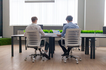 two young businessmen in business clothes sitting in office and discussing project, office workers colleagues planning report and pointing at statistics