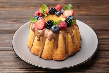 Tasty Bundt cake with berries, chocolate and mint on wooden table, closeup