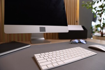 Modern computer, notebook and glasses on desk in office, selective focus