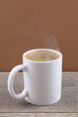 Aromatic coffee in cup on wooden table against brown background, closeup. Mockup for design