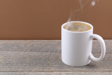 Aromatic coffee in cup on wooden table against brown background, closeup. Space for text