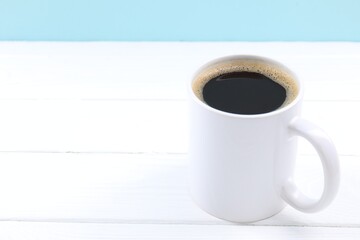 Aromatic coffee in cup on white wooden table against light blue background, closeup. Space for text