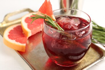Tasty cocktail with grapefruit, ice cubes and rosemary on white table, closeup