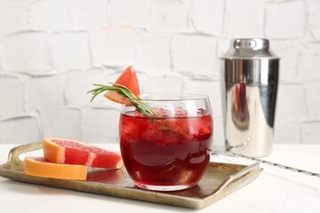Tasty cocktail with grapefruit, ice cubes, rosemary and shaker on white table, closeup