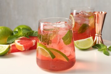 Tasty cocktail with ice cubes, lime and grapefruit on white table, closeup