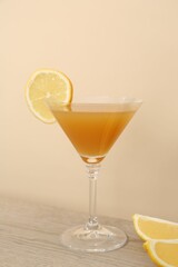 Tasty lemon cocktail in glass and fresh fruit pieces on wooden table against beige background