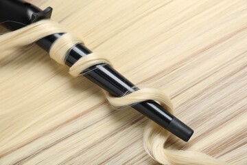 Naklejka premium Curling iron with shiny blonde hair, closeup
