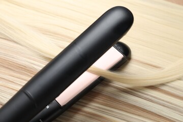 Modern flat iron on shiny blonde hair, closeup