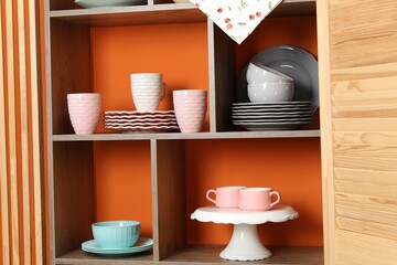 Shelving unit with different dishware and cups near orange wall indoors