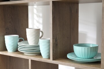 Different plates and cups on shelves near white wall indoors, closeup