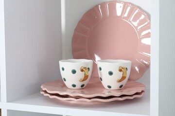 Clean plates and cups on shelf indoors, closeup