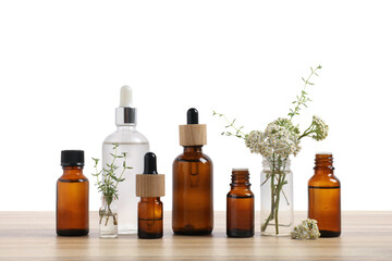 Bottles of essential oils and different herbs on wooden table against white background