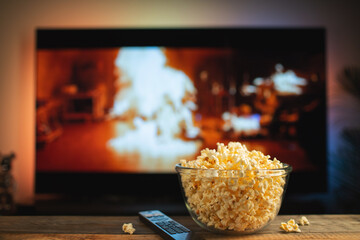 A glass bowl of popcorn and remote control in the background the TV works. Evening cozy watching a...