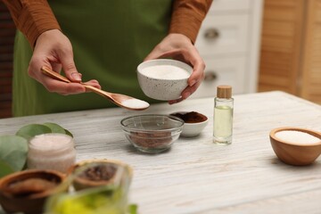 Making natural scrub. Woman adding sugar into bowl at white wooden table, closeup