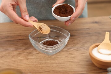 Making natural scrub. Woman adding coffee into bowl at wooden table, closeup