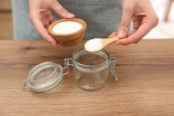 Making natural scrub. Woman adding sugar into jar at wooden table, closeup