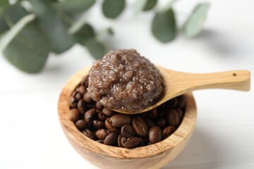 Natural body scrub in spoon, coffee beans and eucalyptus branches on white table, closeup