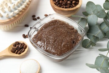 Natural body scrub in glass bowl, ingredients and brush on white wooden table, closeup