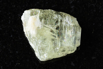 sample of raw hiddenite mineral on black granite