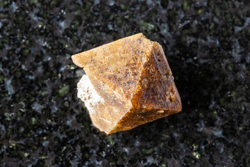 sample of rough zircon crystal on black granite