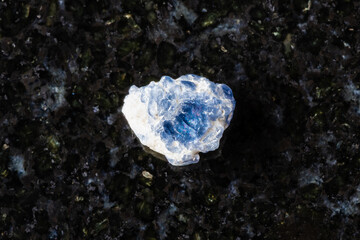 sample of raw blue spinel crystal on black granite