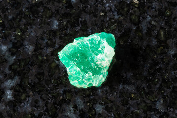 sample of rough emerald mineral on black granite