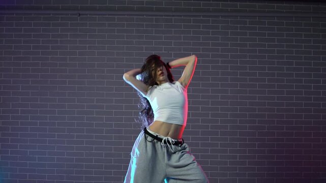 young crazy girl dancing hip hop against wall background in neon lighting, female choreographer moving to music and performing jazz funk in dance studio
