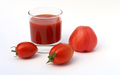 A glass of tomato juice and three tomatoes.