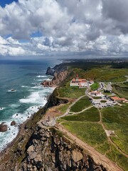 4K Aerial Drone Footage of a Rugged Coastal Landscape Featuring a Lighthouse, Ocean Waves, Cliffs, and Green Hills Captured in Natural Daylight