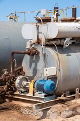 Industrial oil pump with electric motor connected to weathered metal tank, realistic style, on sandy ground, concept of heavy machinery operation