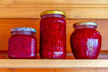 Homemade raspberry jam in glass jars on a wooden shelf.