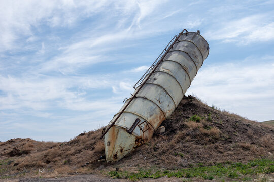 Rusty abandoned silo leaning on a grassy hill under a partly cloudy sky. industrial decay and abandonment