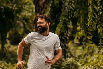 Obraz premium Happy bearded man running in green park enjoying exercise outdoors