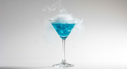 A blue cocktail in a martini glass with white smoke on top against a white background in a studio shot