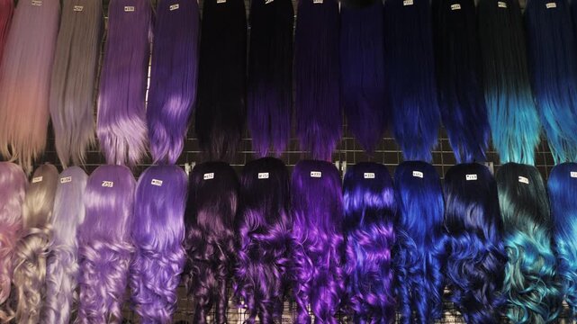 Showcase of natural colorful wigs in different colors fixed on the metal wig holders in beauty salon. Asian comic shop.