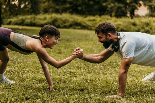 Sporty couple doing plank exercise and shaking hands in park