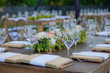 Wooden table decorated with crystal glasses and floral centerpiece, set outdoors for a wedding or elegant celebration.