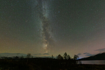 The Northern Lights and Milky Way above the mountains near Dovrefjell National Park, Norway, reflecting in the water.