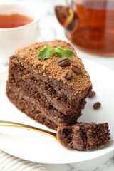 Piece of delicious chocolate cake with coffee beans, mint and fork on table, closeup