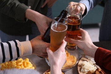 Friends clinking glasses of beer at table, closeup
