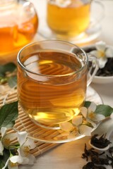 Tasty jasmine tea in cup, dry leaves and flowers on white wooden table, closeup