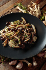 Fried shimeji mushrooms with thyme and garlic on a black plate.