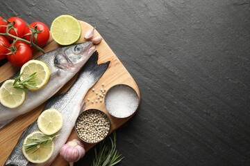 Fresh raw seabass fish with spices on black table, top view and space for text. Seafood delicacies