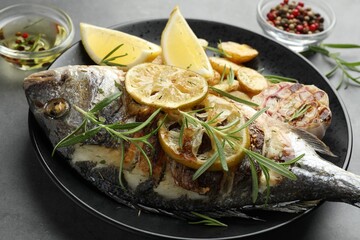 Tasty roasted dorado fish with potatoes, rosemary and lemon on grey table, closeup. Homemade seafood dish