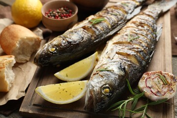 Tasty roasted seabass fish served with bread, rosemary and lemon on wooden table, closeup. Homemade seafood dish