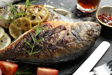 Tasty roasted dorado fish served on black table, closeup. Homemade seafood dish