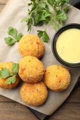 Delicious fried croquette balls with parsley and sauce on wooden table, top view