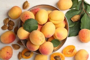 Fresh ripe apricots in bowl and green leaves on white wooden table, flat lay