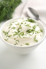 Delicious yogurt in bowl and dill on white table, closeup