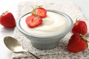 Delicious yogurt in bowl, strawberries and spoon on table, closeup